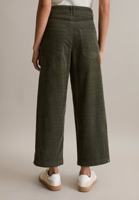 Olivengrüne weite Hose aus strukturiertem Material mit zwei Gesäßtaschen und umgeschlagenen Säumen, kombiniert mit weißen Sneakers.