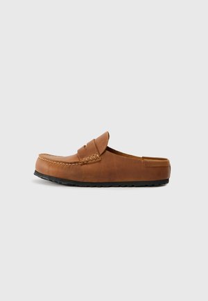 Brun skinn slip-on loafer med svart gummisåle, mokasinsøm og en dekorativ stropp over overdelen.