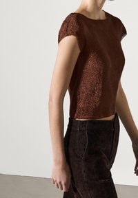 Ruskea uritettua neuletta crop-topia, jossa on lyhyet hihansuut. Yhdistetty tummiin housuihin. Sileä pinta ja tiukka malli. Minimalistinen tyyli puhtain linjoin.