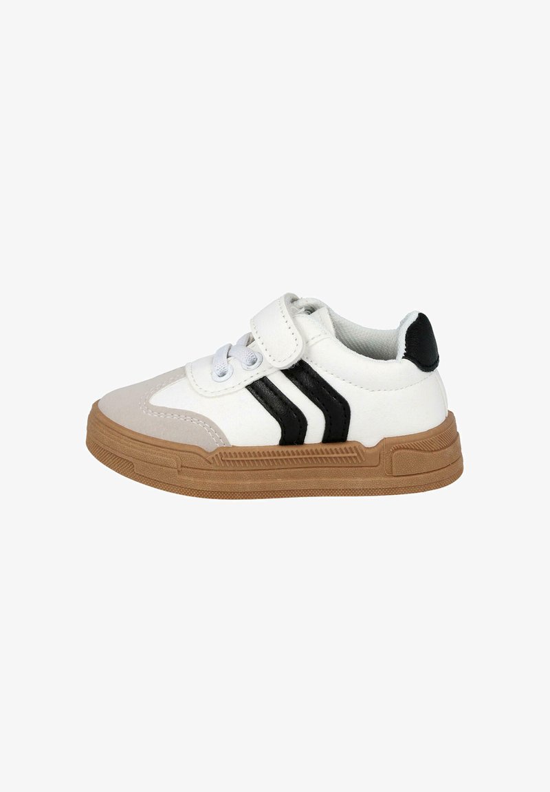 Zapatilla blanca con rayas negras y una correa de velcro. Presenta una suela de goma marrón texturada y un upper sintético liso.