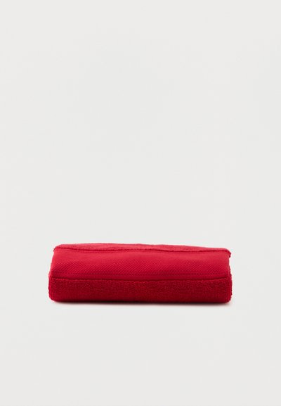 Foldet rødt håndklæde lagt fladt mod en neutral baggrund, der viser tekstur og rene kanter.