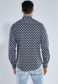Langarmhemd in einem schwarz-weißen geometrischen Muster. Mit einem klassischen Kragen, Knopfleiste und abgerundetem Saum. Hergestellt aus leichtem Stoff.
