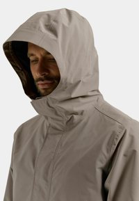 Leichte, beige wasserdichte Jacke mit Kapuze, ausgestattet mit hohem Kragen, glatter Textur und dezenten Steppnähten.