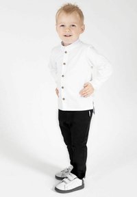 Biała koszula z długim rękawem zapinana na guziki, czarne spodnie oraz szaro-białe trampki. Prosty fason i dopasowany krój.