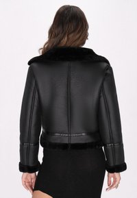 Jachetă din piele neagră cu guler și mansete din blană sintetică, design scurt, finisaj texturat. Include detalii fine de cusătură și o siluetă elegantă.