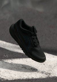 Schwarzer Sportschuh mit Mesh-Obermaterial, das eine strukturierte Oberfläche und ein Logo an der Seite aufweist. Leichtgewichtig, mit gepolsterter Sohle und Schnürsenkeln.