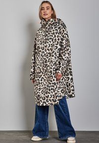 Impermeable con estampado de leopardo y capucha, que cuenta con un corte relajado, mangas largas y una tela de fácil cuidado. Usado sobre jeans de pierna ancha.