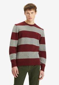 Maroon and gray striped sweater, crew neckline, ribbed cuffs and hem, soft texture, worn over green pants. Small logo on chest.