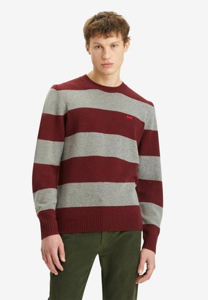 Sweter w paski w kolorach bordowym i szarym, okrągły dekolt, ściągacze przy rękawach i dolnym końcu, miękka tekstura, noszony na zielonych spodniach. Małe logo na klatce piersiowej.