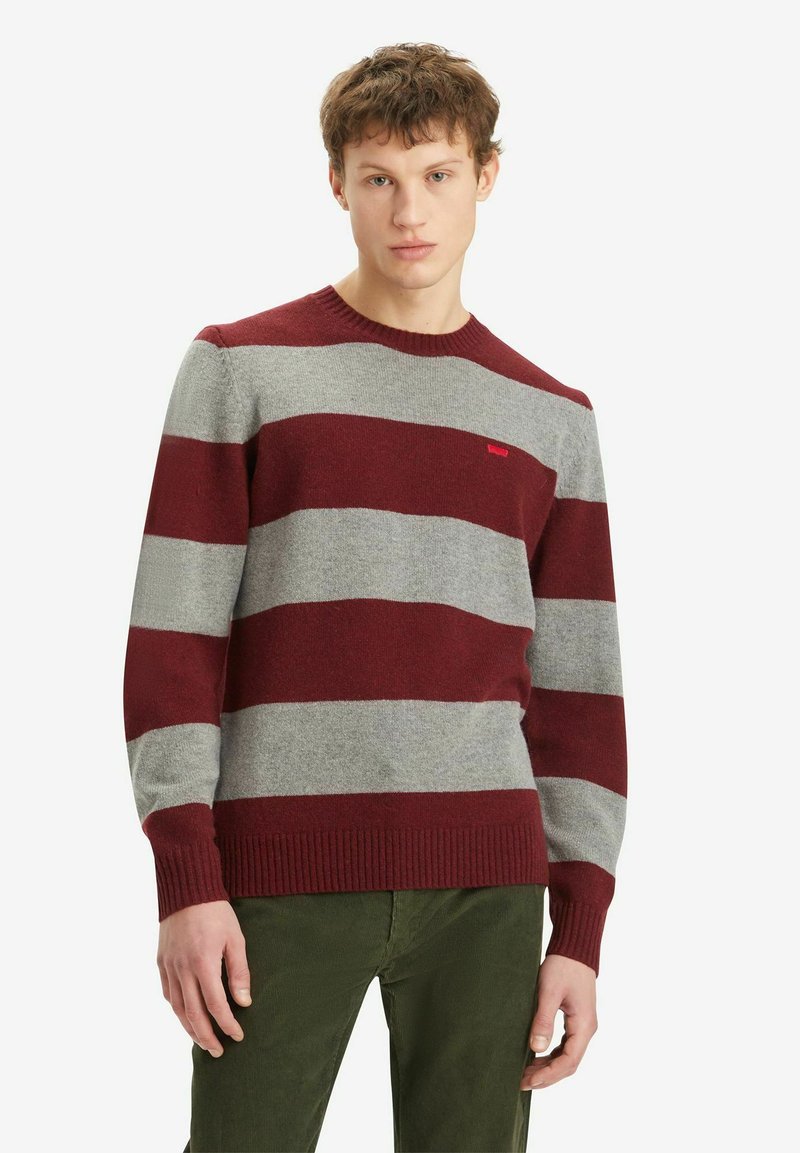 Sweater a righe bordeaux e grigio, colletto a giro, polsini e orlo a coste, texture morbida, indossato su pantaloni verdi. Piccolo logo sul petto.