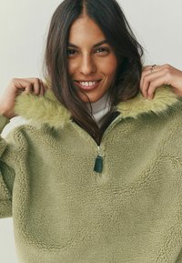 Heleroheline fliisist pullover kunstkarvase krae, poollukuga disaini ja tekstuurse kangaga. Krae ja varrukad on pehmete, kohevate detailidega.