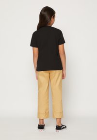 Camiseta negra de manga corta, pantalones anchos amarillos y zapatillas negras. La camiseta tiene un escote redondo; los pantalones tienen puños doblados.