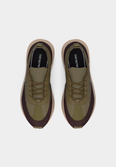 Ζευγάρι αθλητικών παπουτσιών σε ελαιί πράσινο και καφέ με κορδόνια και μπεζ σόλες, με το λογότυπο Emporio Armani εμφανές στο εσωτερικό του παπουτσιού.