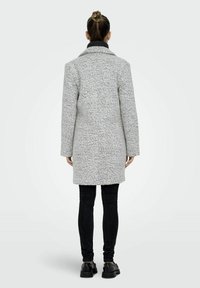 Manteau texturé gris avec col, manches longues, design mi-long, associé à un pantalon noir ajusté et des chaussures noires épaisses.
