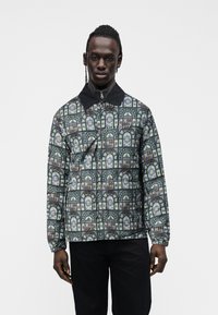 Casaco pulôver estampado com design de vitral floral escuro, gola preta e fecho de correr, com punhos elásticos.