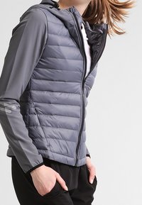 Harmaa toppatakki, jossa on istuva malli, vetoketjukiinnitys ja huppu. Takissa on vaakasuora tikkaus ja kontrastiväriset harmaat hihat.