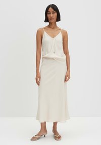 Cream silk camisole with thin straps, layered over a matching long skirt. The outfit features a smooth texture and a flowing silhouette.
