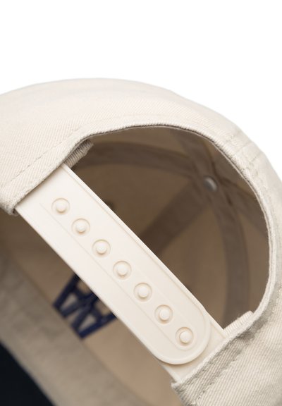 Casquette beige à visière courbée, fabriquée en toile. Dotée d'une sangle en plastique ajustable avec des trous circulaires pour le réglage de la taille.