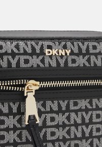 Borsa nera con zip che presenta il logo DKNY in un motivo intessuto bianco, accentuata da hardware dorato e dettagli in pelle liscia.