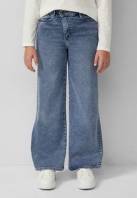 Hellblaue Denim-Jeans mit weitem Bein und fransigen Säumen, Fünf-Taschen-Design und mittelhohem Bund. Kombiniert mit weißen Sneakers.