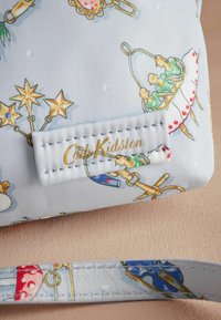 Ljusblå tygväska med spännande mönster av olika föremål, med en guldig logotags och en matchande rem. Slät textur.