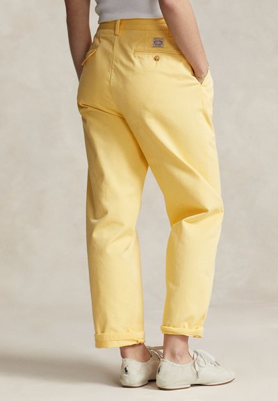 Gula bomullsbyxor med lös passform, uppvikta fållar och bakfickor. Matchas med ljusa skor.