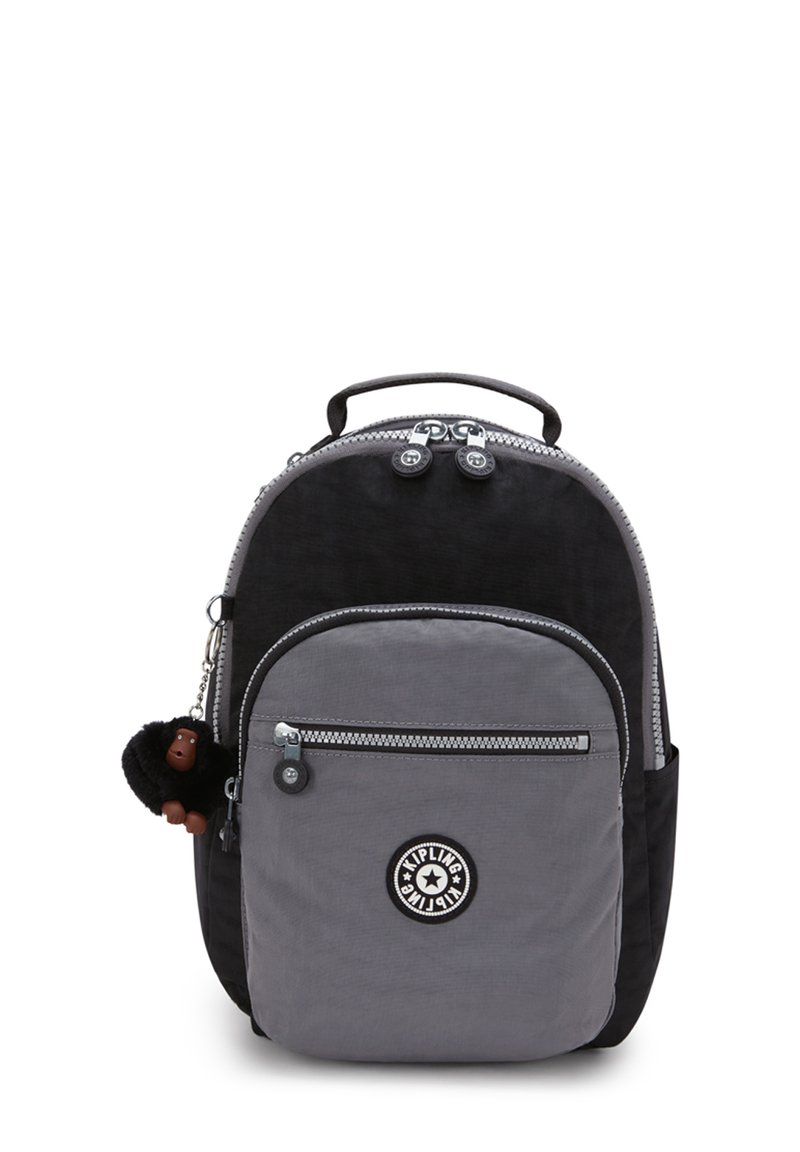 Schwarzer und grauer Nylon-Rucksack in runder Form, mit Reißverschluss-Taschen und einem pelzigen Affen-Schlüsselanhänger. Mit einem Logo-Patch auf der Fronttasche.