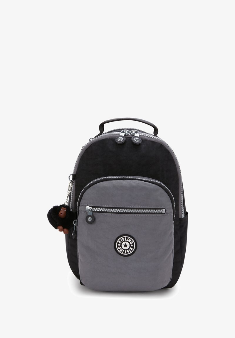 Schwarzer und grauer Nylon-Rucksack in runder Form, mit Reißverschluss-Taschen und einem pelzigen Affen-Schlüsselanhänger. Mit einem Logo-Patch auf der Fronttasche.