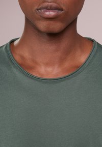 Grön bomullströja med rund halsringning, slät textur och figurnära design. Inga synliga mönster eller hårdvarudetaljer.