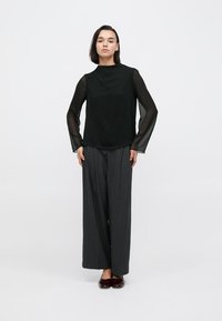 Μαύρο τοπ με διάφανα μακριά μανίκια, συνδυασμένο με γκρι παντελόνι φαρδιάς γραμμής και γυαλιστερά μπορντό παπούτσια. Απλή σιλουέτα και απαλές υφές.