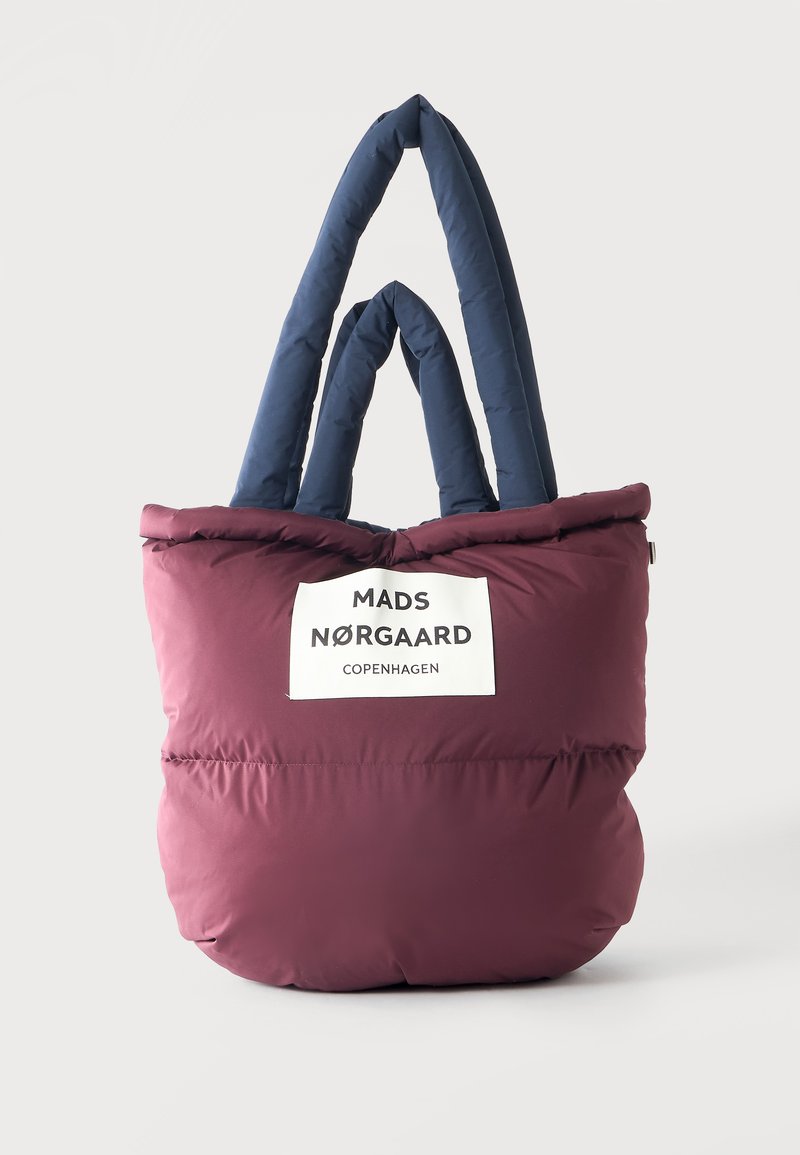 Sac cabas bordeaux matelassé avec des poignées matelassées bleu marine et une étiquette blanche portant l'inscription Mads Nørgaard Copenhagen sur le devant.