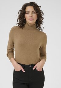 Brązowy sweter z golfem wykonany z miękkiego dzianinowego materiału, z długimi rękawami i ściągaczami, zestawiony z czarnymi spodniami.