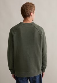 Oliwkowa bluza z raglanowymi rękawami, prążkowanym dekoltem i mankietami. Widok z tyłu ukazuje gładką teksturę i luźny krój.