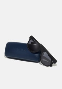 Ochelari de soare negri cu un finisaj mat, având o formă pătrată îndrăzneață. Viniți împreună cu un etui dur albastru, gravat cu logo-ul brandului.