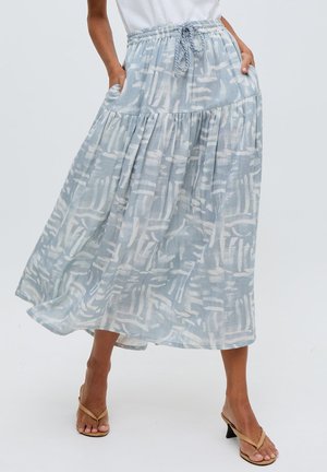 Frau trägt einen fließenden, hellblauen Midirock mit Muster, geschnürter Taille und Bindeband, kombiniert mit beigen Sandalen mit Absatz.