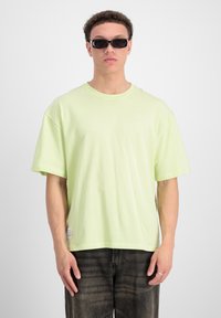 Camiseta XL de color verde claro, hecha de algodón suave, con hombros caídos y cuello redondo. Combinada con pantalones de mezclilla oscuros.