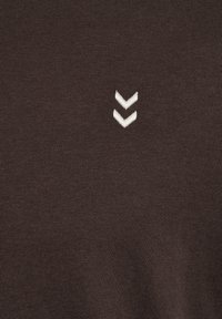 Mørkebrunt stof med en ribbet tekstur. Har to hvide broderede chevron-former, der er justeret lodret.