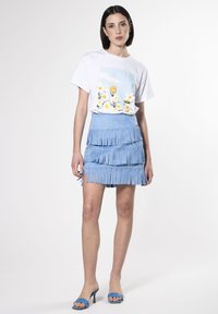 Witte T-shirt met bloemgrafiek, gecombineerd met een lichtblauwe franjerok. De rok heeft meerdere lagen en decoratieve hardwareaccenten.