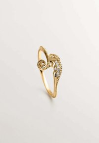 Anillo de oro con forma de caballito de mar, que presenta un detalle texturizado y un acento en espiral. Embellecido con pequeñas piedras preciosas redondas a lo largo de un lado.