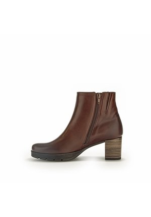 Bottine en cuir marron avec un bout arrondi, fermeture éclair sur le côté et un talon en bois empilé. Texture lisse avec un léger brillant.