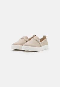 Beige Slipper aus Stoff, mit einer geflochtenen Akzentuierung am Vorderfuß und einer weißen Gummisohle. Leicht und mit glatter Textur.