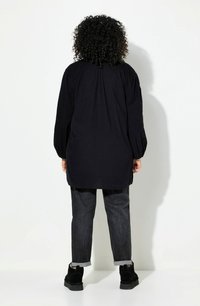 Camicia nera a maniche lunghe con una vestibilità ampia, caratterizzata da una schiena plissettata, abbinata a jeans scuri e stivaletti neri. Design semplice.