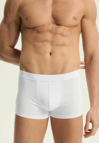 Białe bawełniane bokserki o gładkiej teksturze, dopasowanym kroju i szerokim pasie, z otworem z przodu i krótkimi nogawkami.