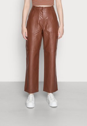 Bruine, hooggetailleerde wijde neplederen broek met voorzakken, gedragen met witte sneakers en een kort gestreept topje.