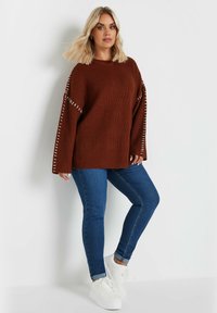 Rostfärgad stickad tröja med vida ärmar och vit sömnad. Matchad med mörkblå jeans och vita sneakers.