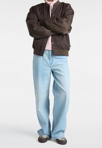 Brązowa pikowana bomberka na jasnoróżowej bluzie z kapturem, w parze z jasnoniebieskimi spodniami dzwonami i ciemnobrązowymi trampkami z wzorzystym akcentem.