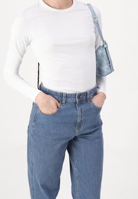 White long-sleeve shirt, blue striped denim pants, and a small blue bag with a strap. The fabric appears smooth and slightly textured.