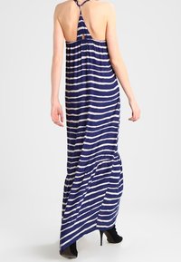 Marinblå och vit randig maxiklänning med halterneck, öppen rygg och samlad midja, med en lätt svalkad silhuett och ankellång fåll.