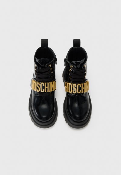 Mustad lakknahk kingad kuldse "Moschino" logo rihmaga, kujulise lõikega, ja külje tõmblukuga. Paks kummist tallaga, ümmargune nina.