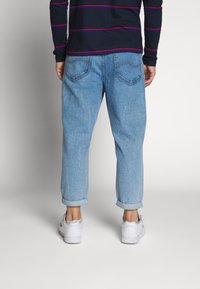 Ljusblå denimjeans med avslappnad passform, synliga bakfickor, uppvikta muddar och sliten textur, kombinerat med vita sneakers.